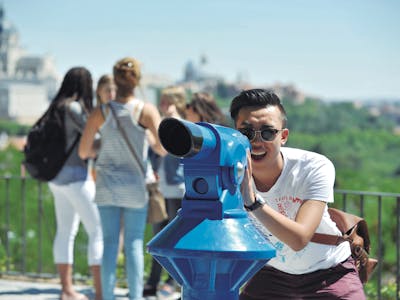 Giovane uomo che guarda attraverso un telescopio da un belvedere a Madrid, Spain, rappresentando un'attività turistica per le vacanze e viste panoramiche della città.