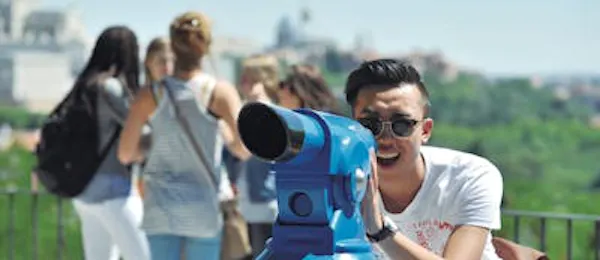 Giovane uomo che guarda attraverso un telescopio da un belvedere a Madrid, Spain, rappresentando un'attività turistica per le vacanze e viste panoramiche della città.