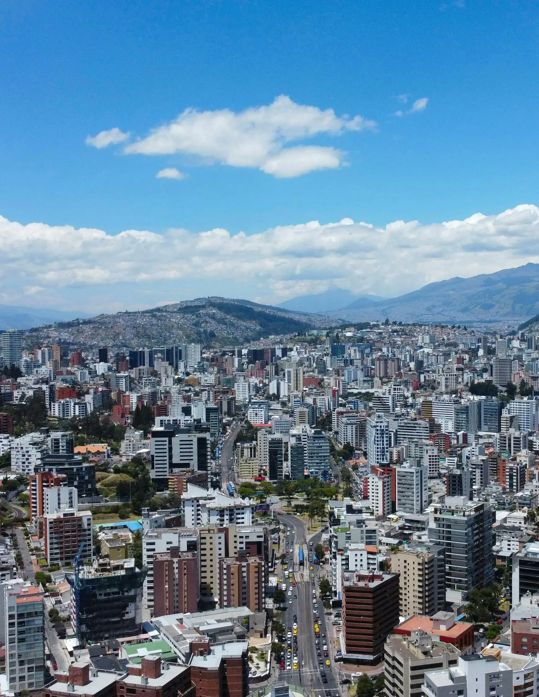 晴れた空の下、山々と近代的な建物に囲まれたキト