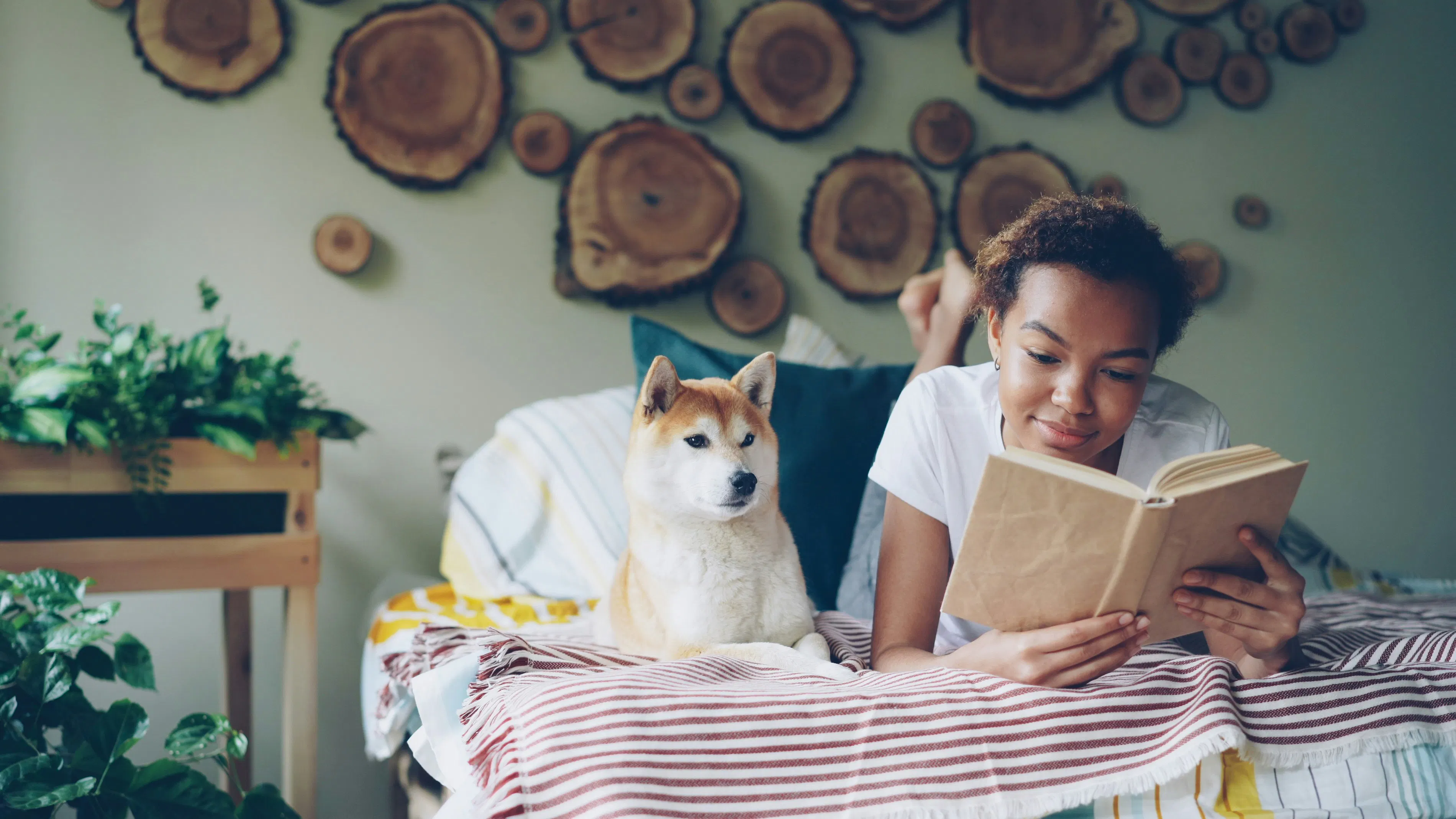 امرأة تقرأ كتابًا مع كلب على السرير.
