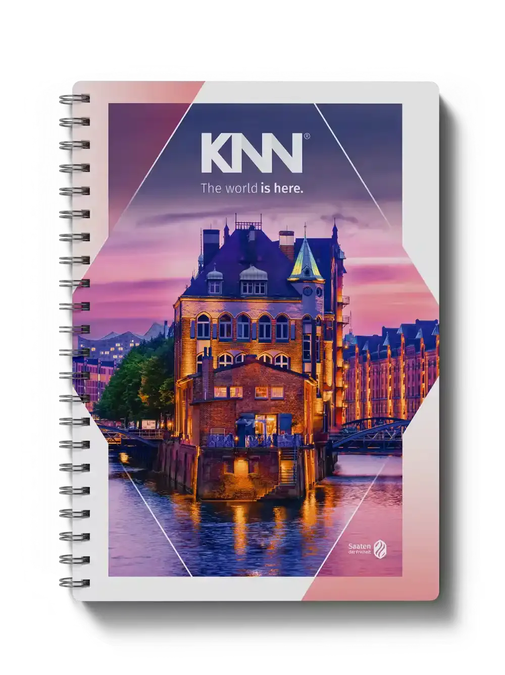 Capa de caderno com a marca KNN e a frase “The world is here.”, mostrando paisagem urbana ao entardecer com prédio iluminado e ponte refletida no rio.