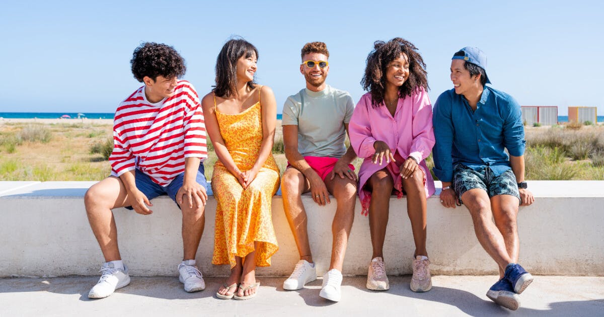 Quatro jovens sentados juntos em um muro, sorrindo e desfrutando de um momento de amizade e descontração.