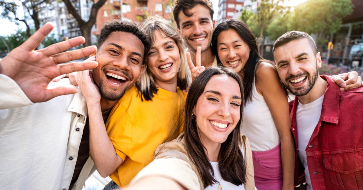 Um grupo de jovens sorrindo e posando juntos para tirar uma selfie em um ambiente descontraído.