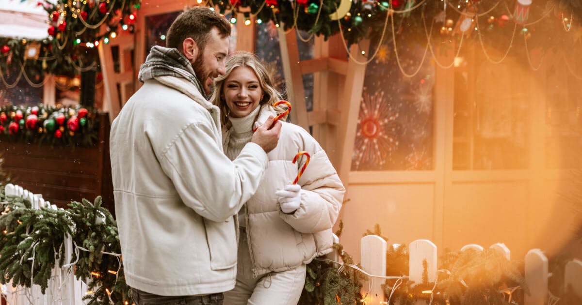 Um casal em pé diante de uma árvore de Natal decorada, transmitindo um clima festivo e de união.