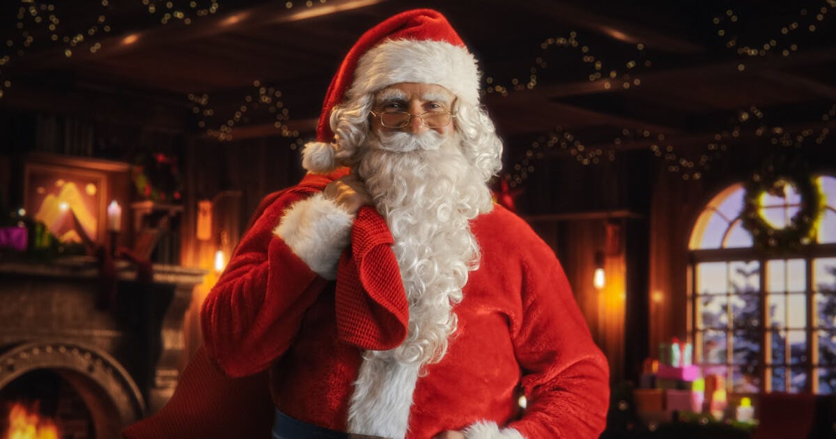 Papai Noel em um traje vermelho, posando em frente a uma lareira acesa, criando um ambiente natalino acolhedor.