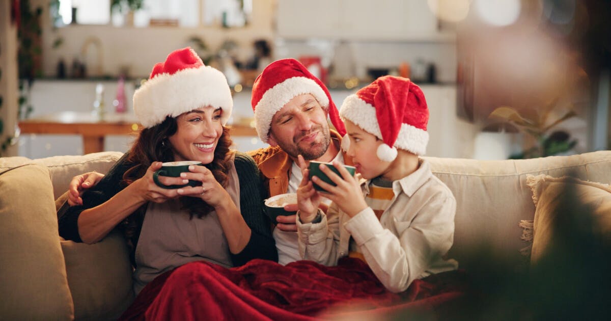 Família reunida no sofá, usando chapéus de Natal, celebrando a época festiva com alegria e união.