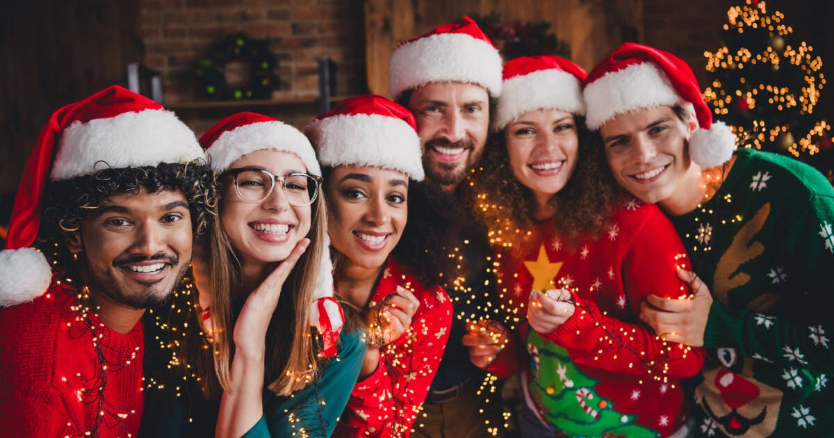 Grupo de pessoas usando suéteres e chapéus de Natal, sorrindo e celebrando a festividade.