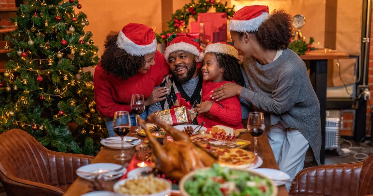 Família reunida, celebrando o Natal com sorrisos, pratos festivos e decoração natalina ao fundo.