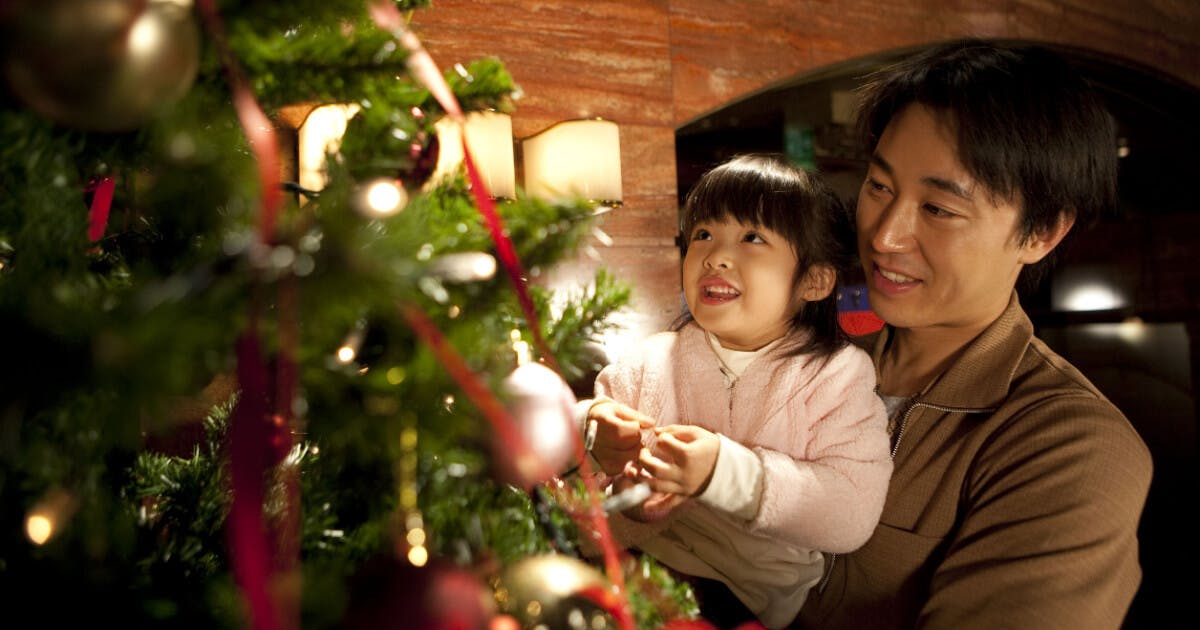 Um homem e uma menina pequena decoram uma árvore de Natal com enfeites coloridos e luzes brilhantes.