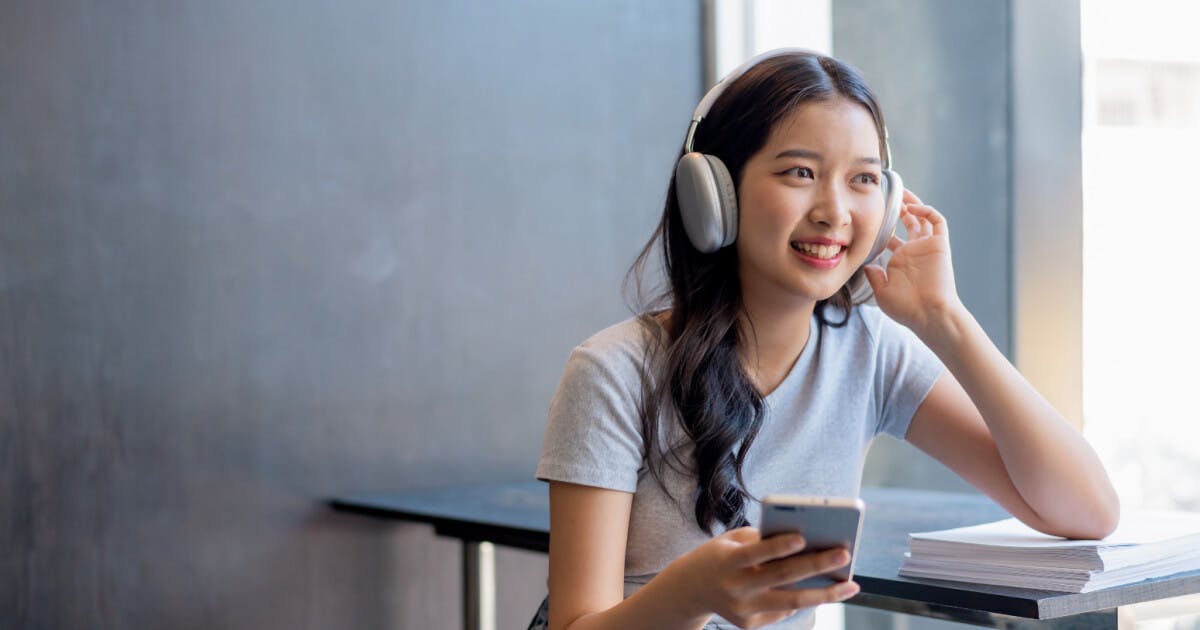 Mulher asiática ouvindo música com fones de ouvido enquanto está sentada à mesa.