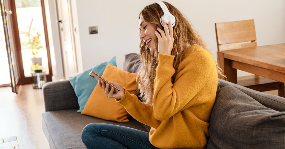 Uma mulher sentada no sofá, usando fones de ouvido, desfrutando de música.