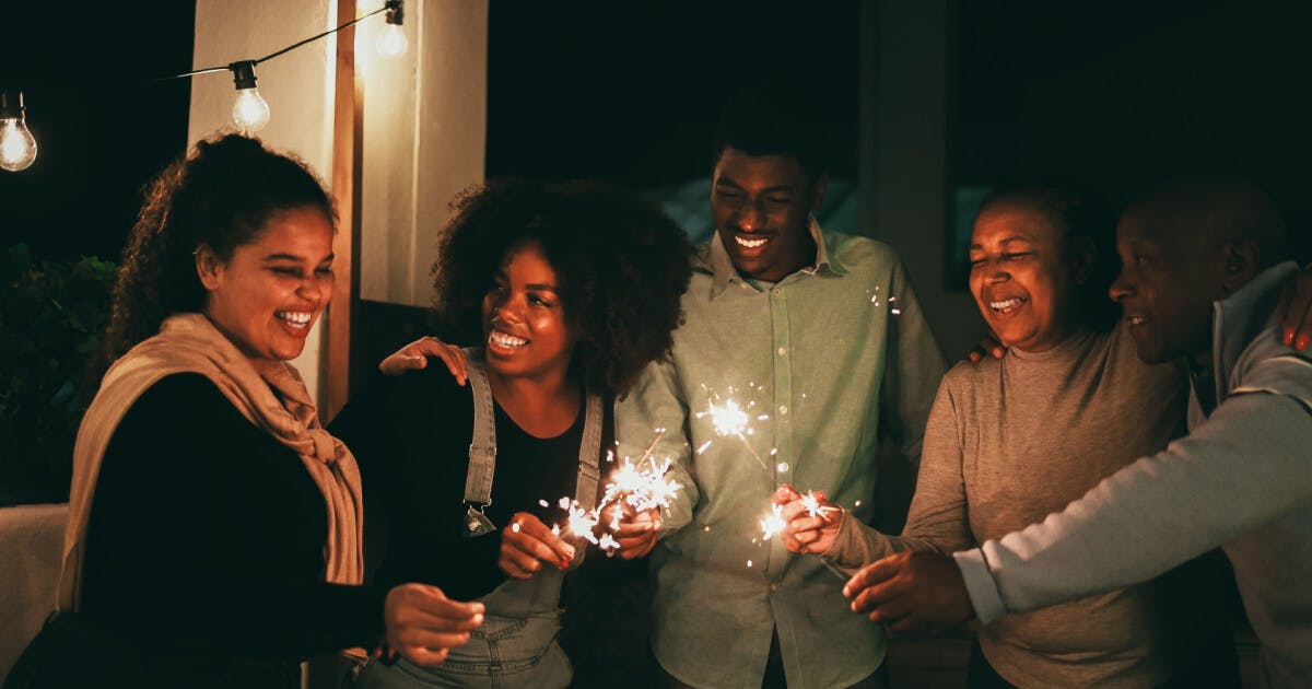 Grupo de amigos sorrindo e segurando fogos de artifício, criando um ambiente festivo e alegre.