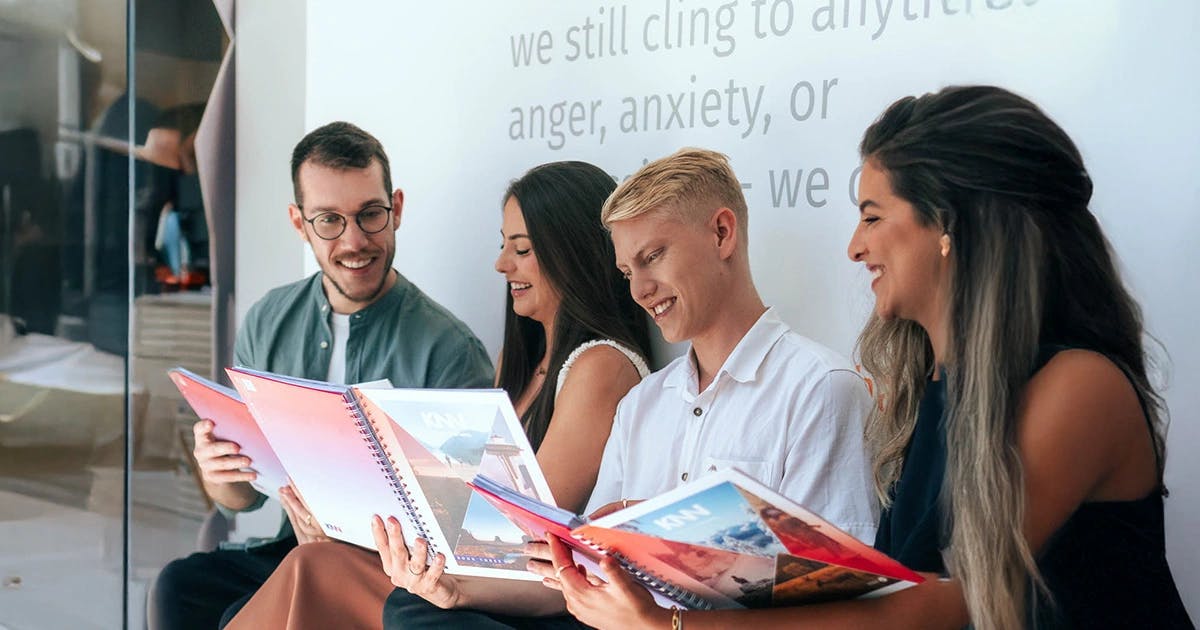 Quatro pessoas folheando os materiais didáticos da KNN Idiomas em um clima descontraído.