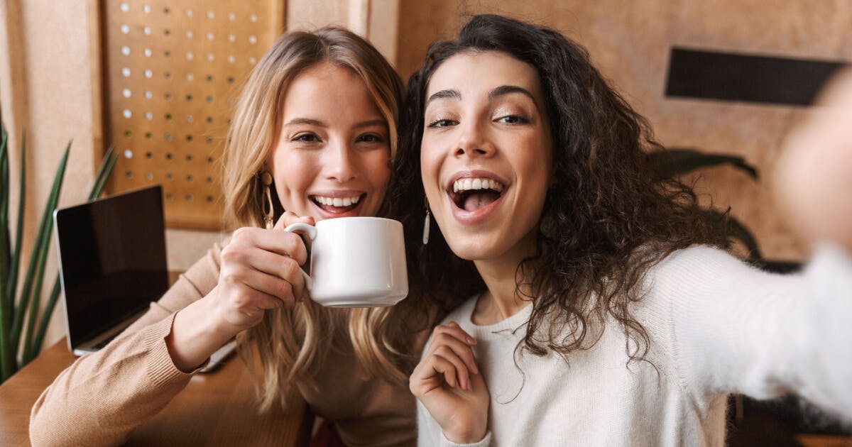 Duas mulheres sorrindo enquanto tiram uma selfie segurando uma xícara de café.