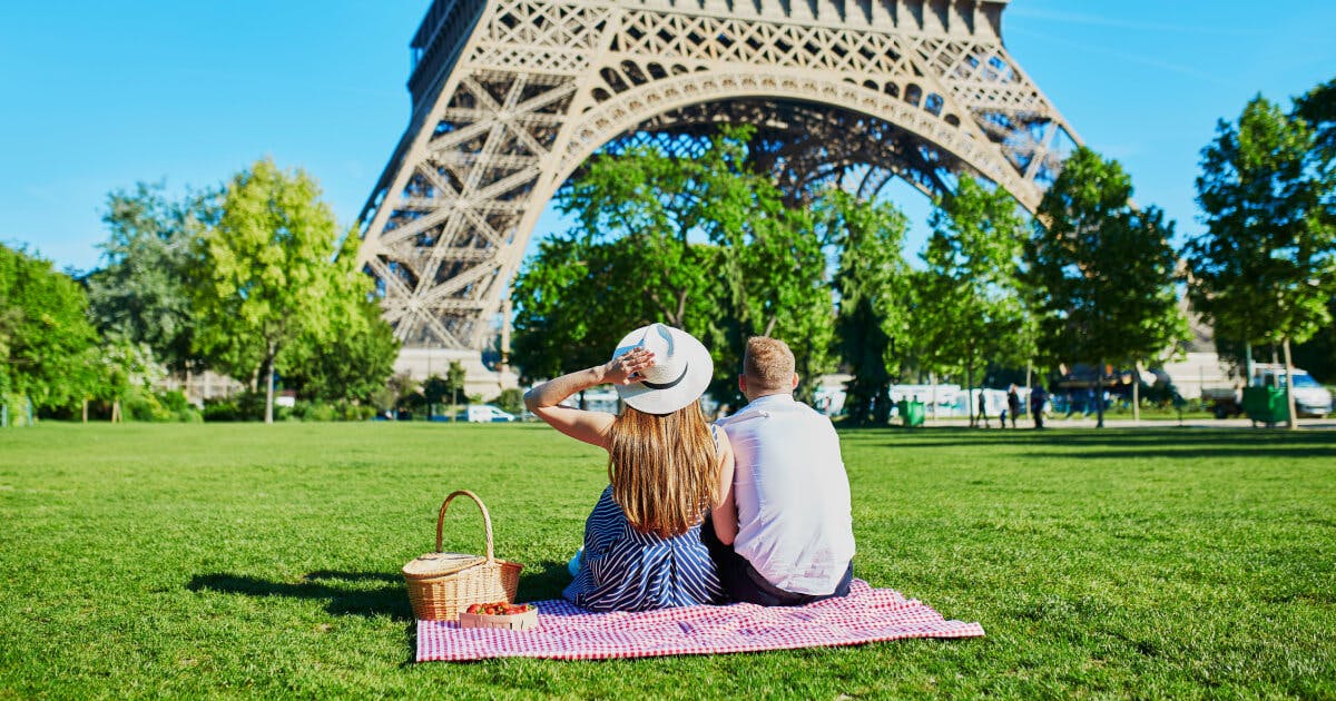 Casal sentado na grama em frente à Torre Eiffel, desfrutando de um momento romântico em Paris.