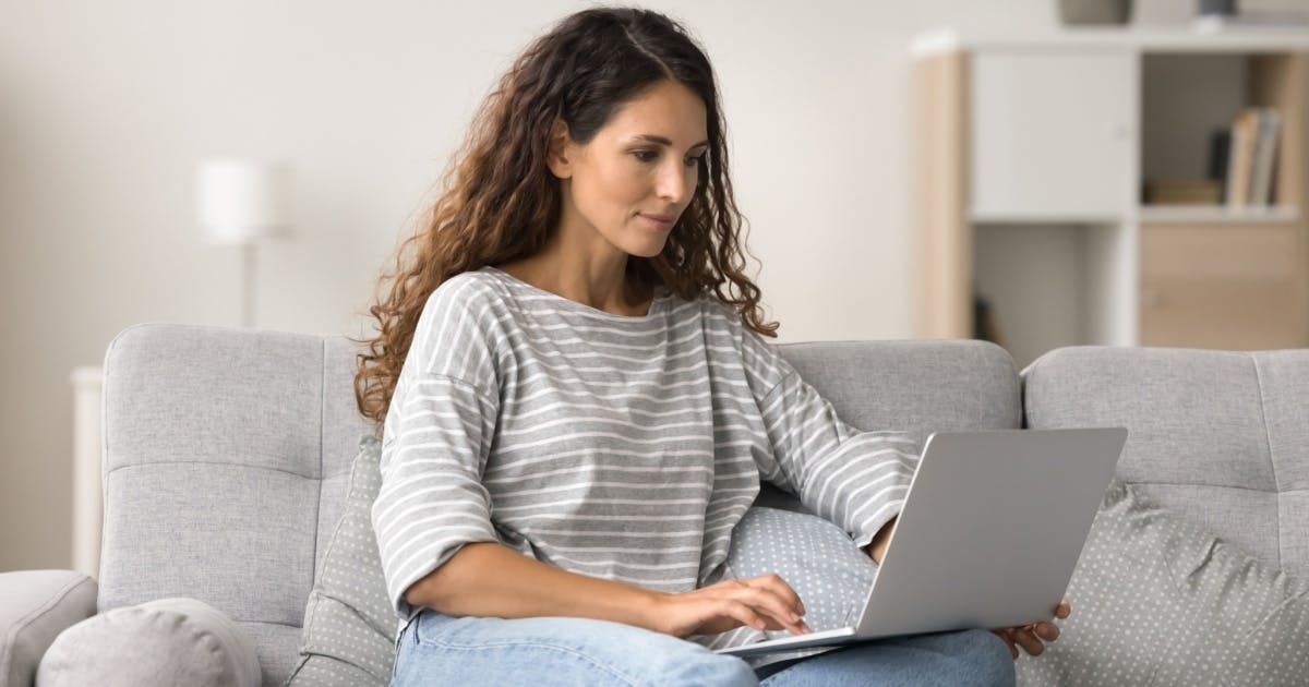 Mulher sentada no sofá e com um notebook no colo.