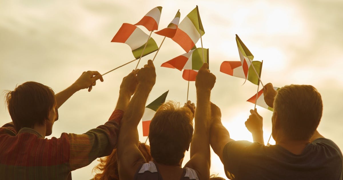 Alunos após aula de italiano acenando bandeiras italianas no ar, celebrando com alegria e entusiasmo em um momento festivo.