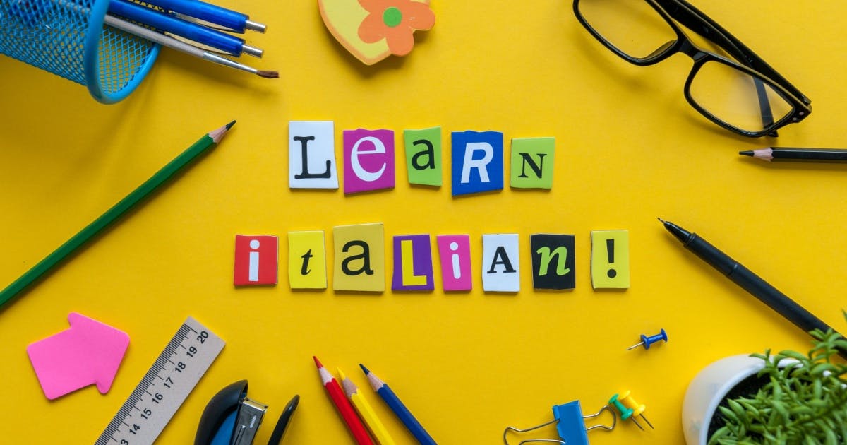 Imagem de papéis coloridos formando a frase "Learn Italian e suprimentos escolares, representando um momento de estudo alegre.