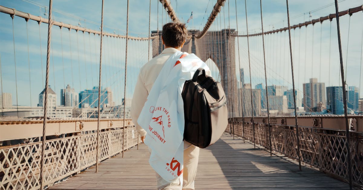 Homem atravessando uma ponte, carregando uma mochila e uma bandeira da KNN Idiomas, em um cenário urbano.