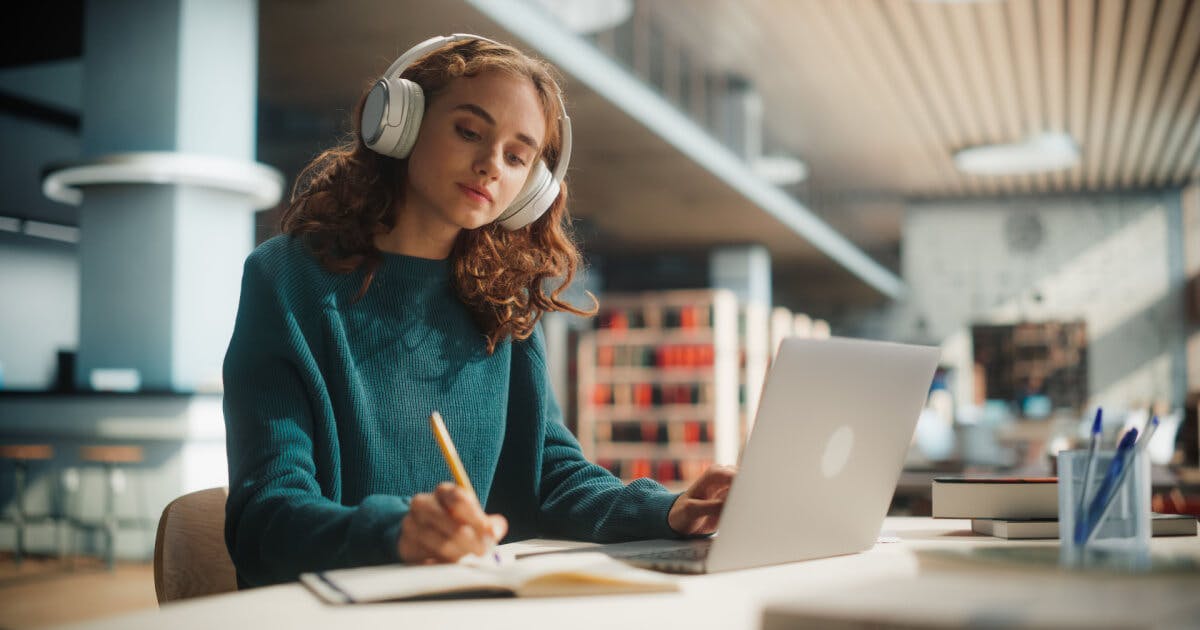 Uma mulher usando fones de ouvido, sentada à mesa com um laptop, concentrada em seu trabalho.