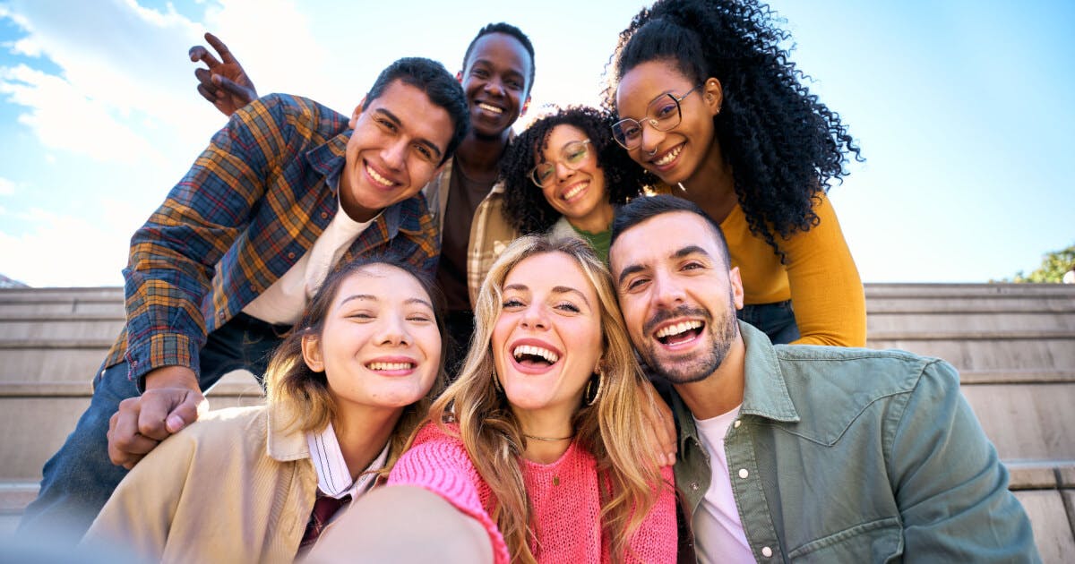 Grupo de jovens sorrindo e tirando uma selfie em um ambiente descontraído.