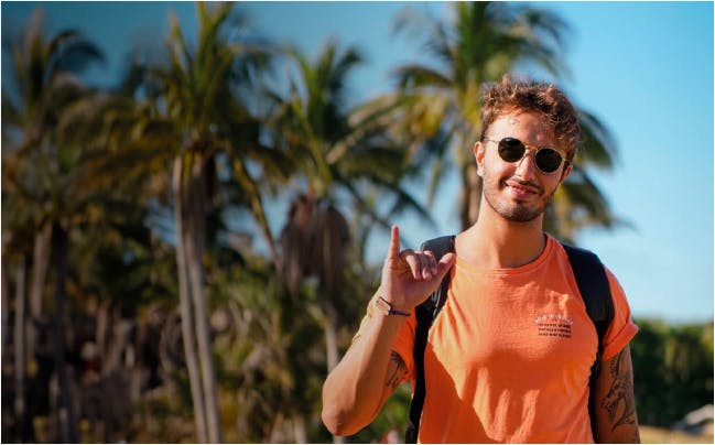 Gean Skrebsky, diretor de marketing da KNN Idiomas de óculos escuro, camiseta laranja e fazendo o símbolo da hang loose.