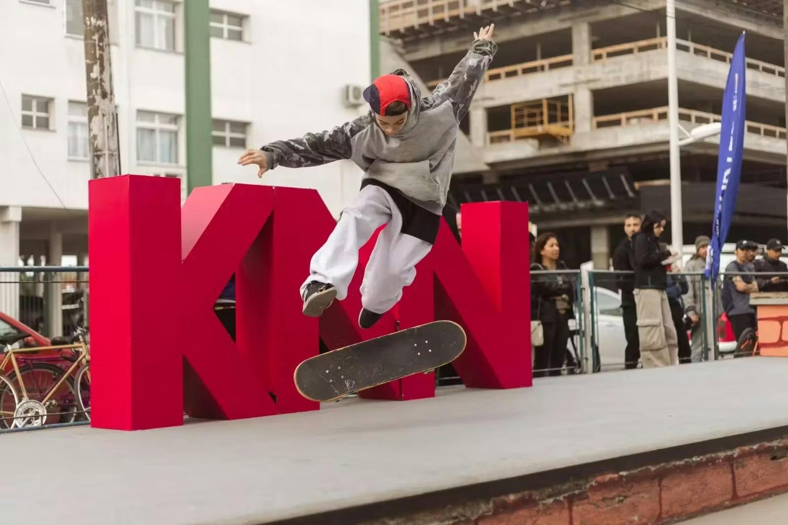 Homem fazendo uma manobra no skate em frente a logo da KNN