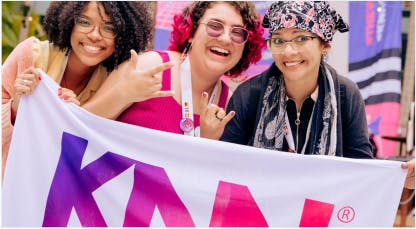 Três mulheres sorrindo com a bandeira da KNN