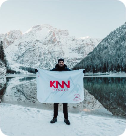 Imagem de uma pessoa segurando a bandeira da KNN. Neve e montanhas ao fundo.