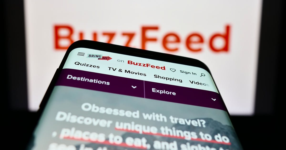 Capa do site "BuzzFeed" sendo mostrada em uma tela de smartphone com a logo da mesma no fundo.