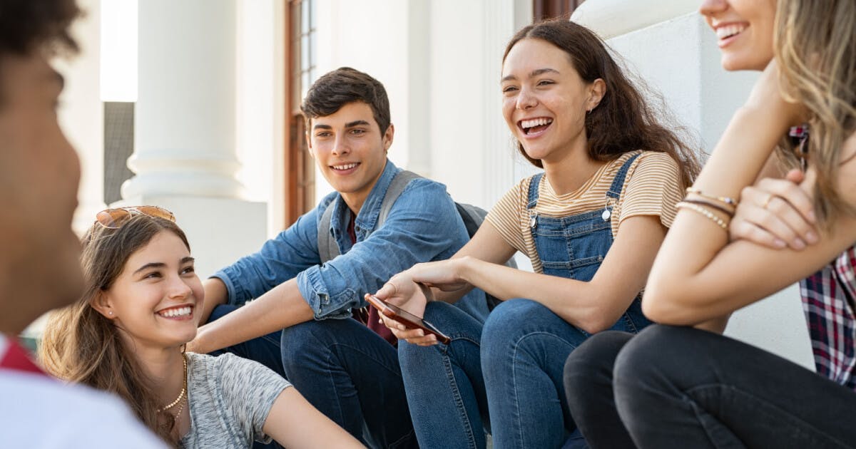 Quatro jovens sentados em degraus, conversando animadamente entre si, em um ambiente descontraído e amistoso.