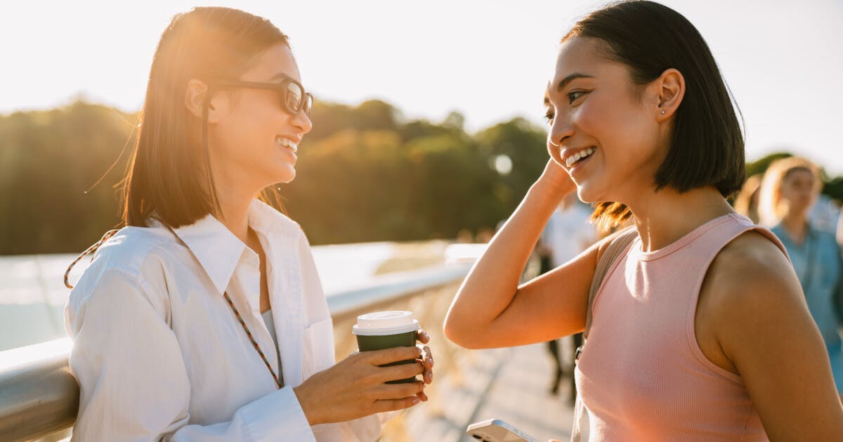 Duas mulheres conversando e sorrindo enquanto estão em pé sobre uma ponte.