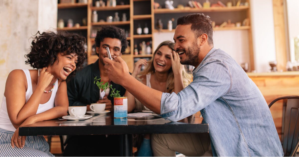 Grupo de amigos conversando animadamente em um café, rodeados por mesas e xícaras de café.