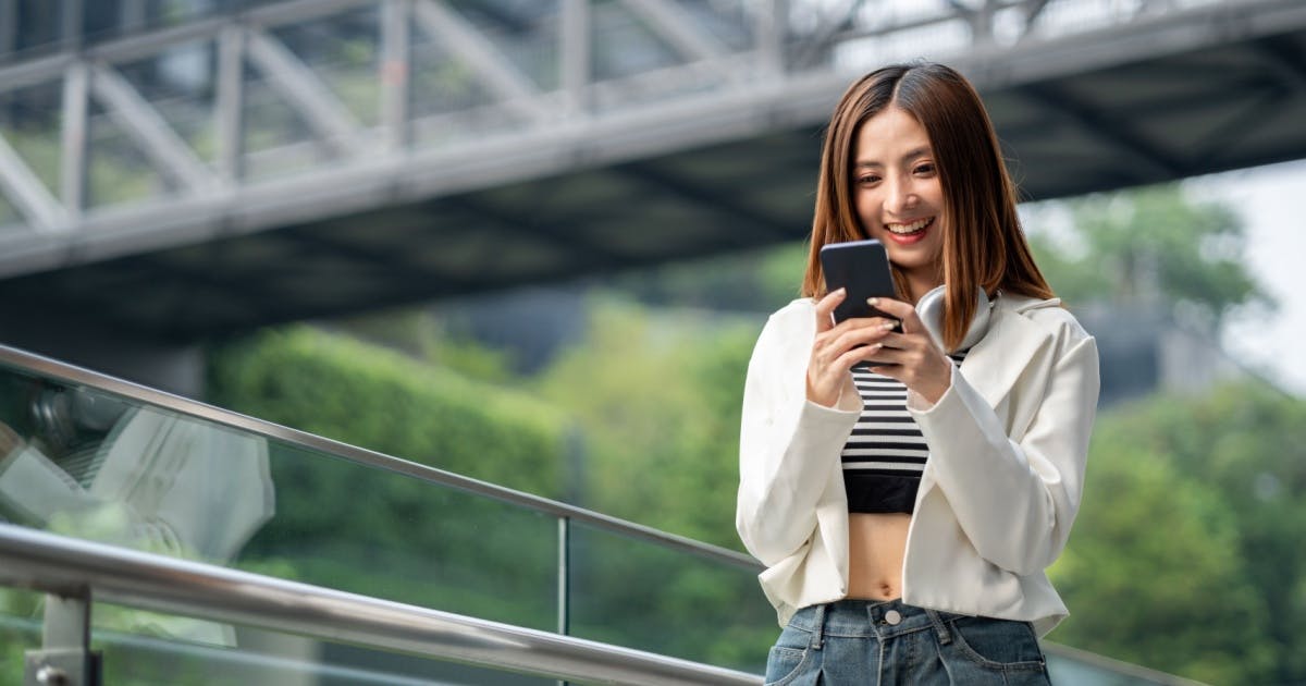 Uma mulher oriental sorrindo olhando para um smartphone.