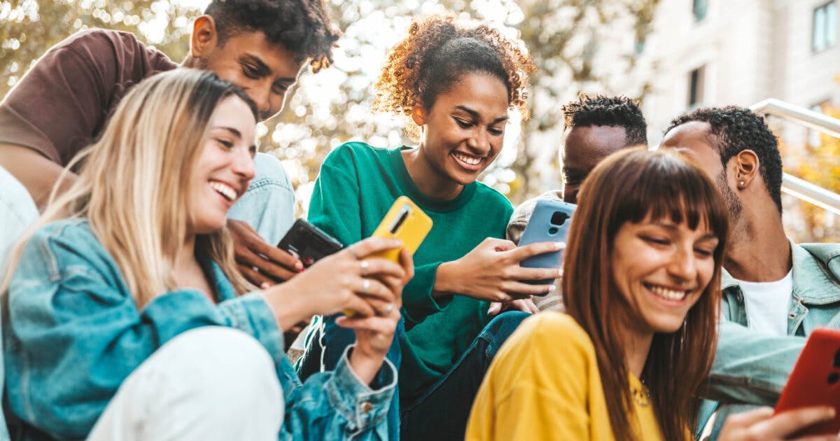 Grupo de jovens sentados em degraus, concentrados em seus celulares, em um ambiente descontraído e urbano.