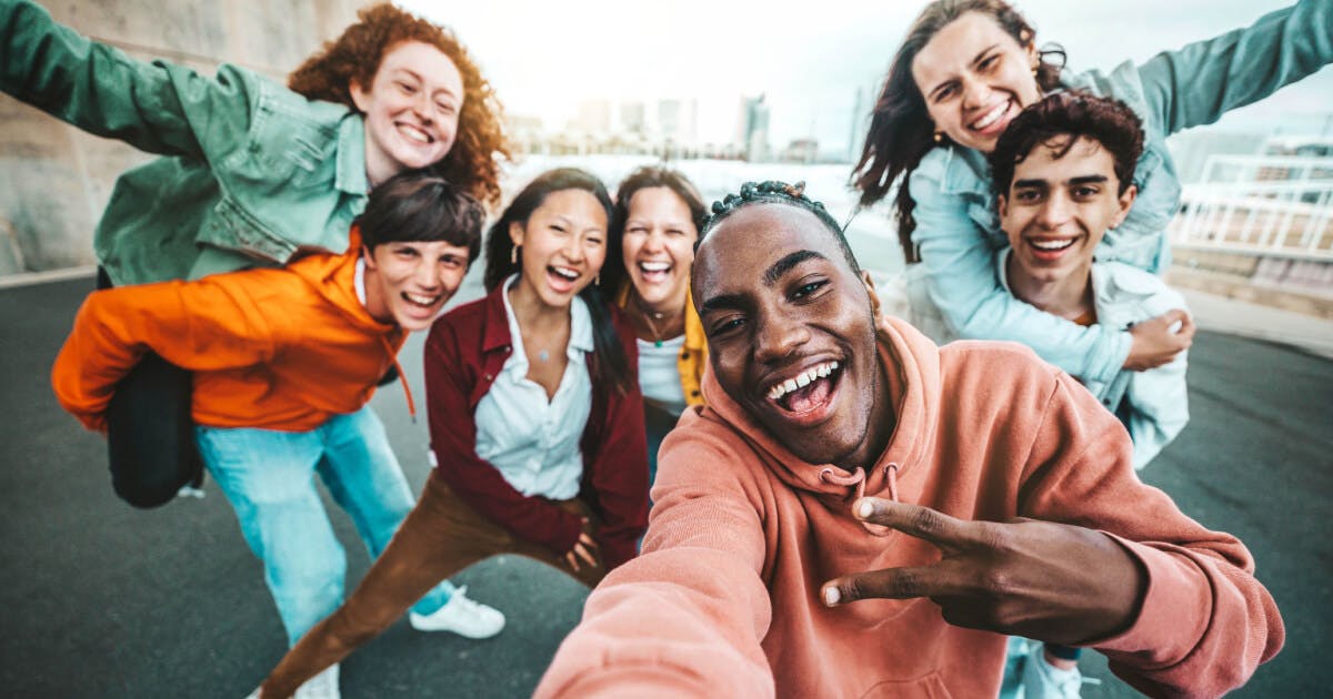 Grupo de jovens sorrindo e tirando uma selfie em um ambiente descontraído.