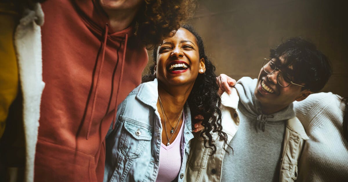 Grupo de jovens sorrindo e rindo juntos, transmitindo alegria e camaradagem em um ambiente descontraído.