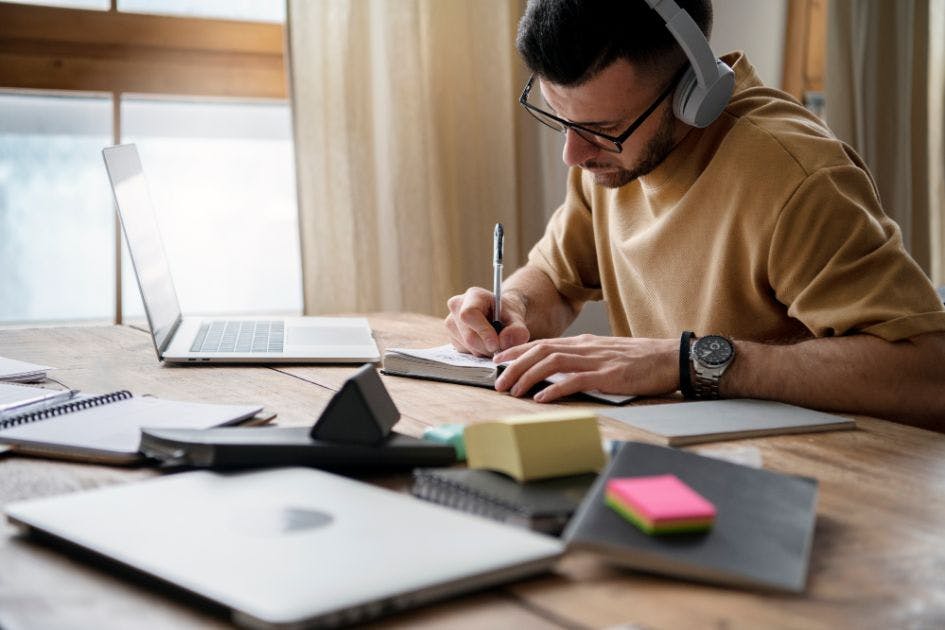 Um homem de óculos estudando e com um fone de ouvido.