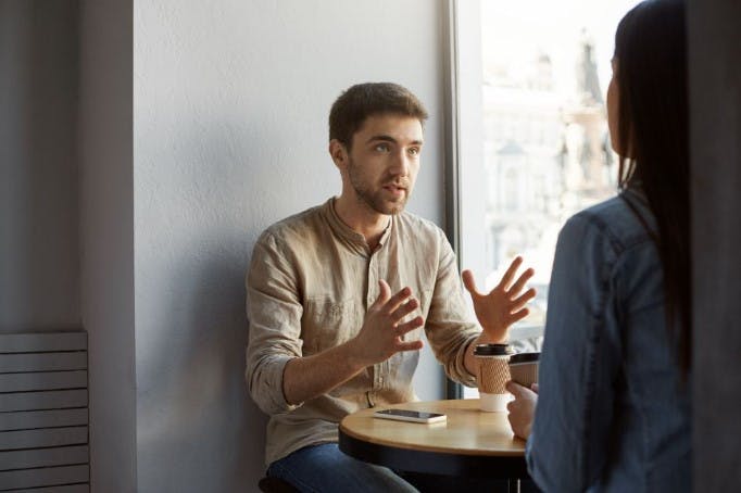 Um homem falando com uma mulher com um copo de café na mão.