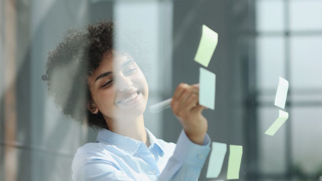 Mulher com uma caneta escrevendo em um post-it.