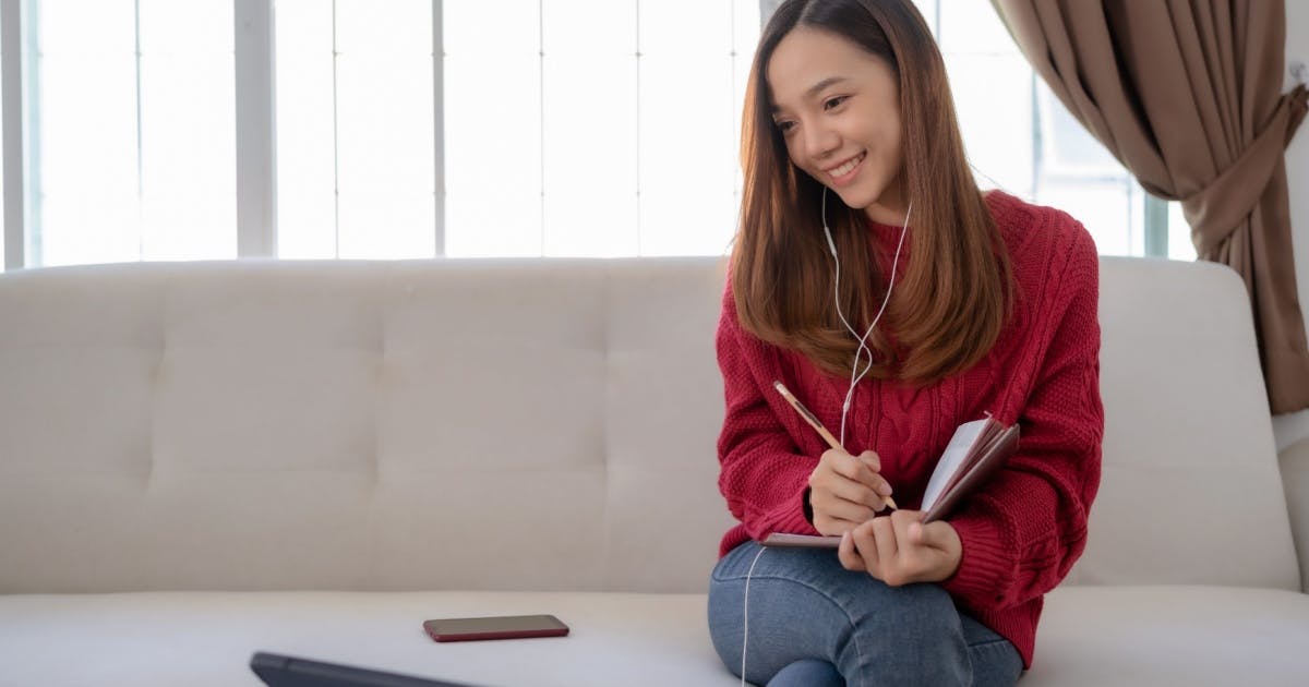 Mulher com um fone de ouvido e anotando em um caderno.