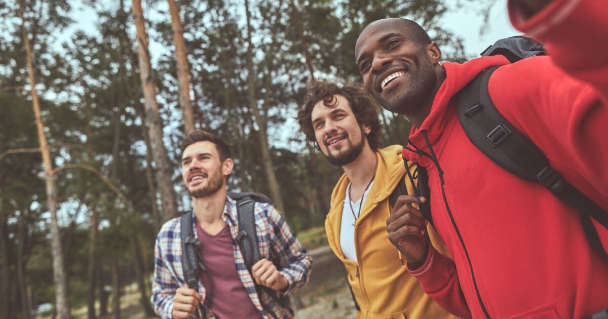 Três homens com mochilas tirando uma selfie juntos em um ambiente ao ar livre.