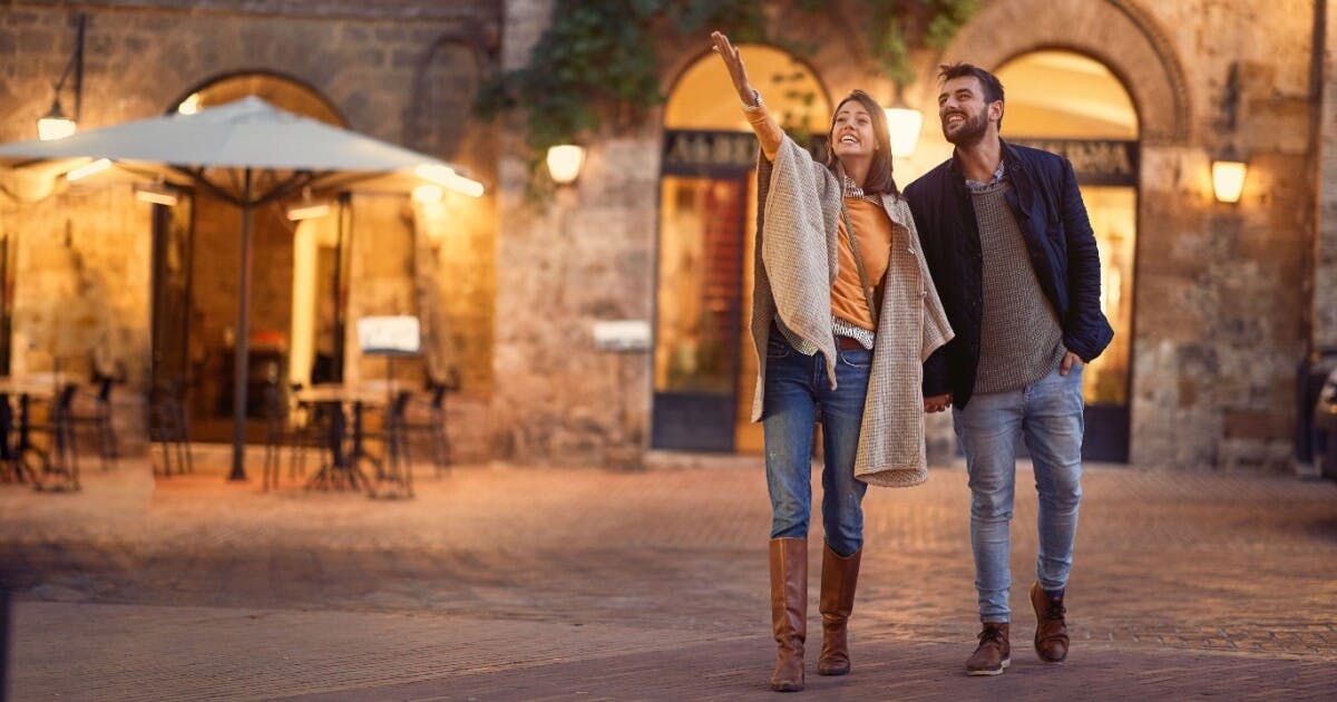 Casal caminhando pela rua à noite, iluminados por luzes urbanas, criando uma atmosfera romântica e tranquila.