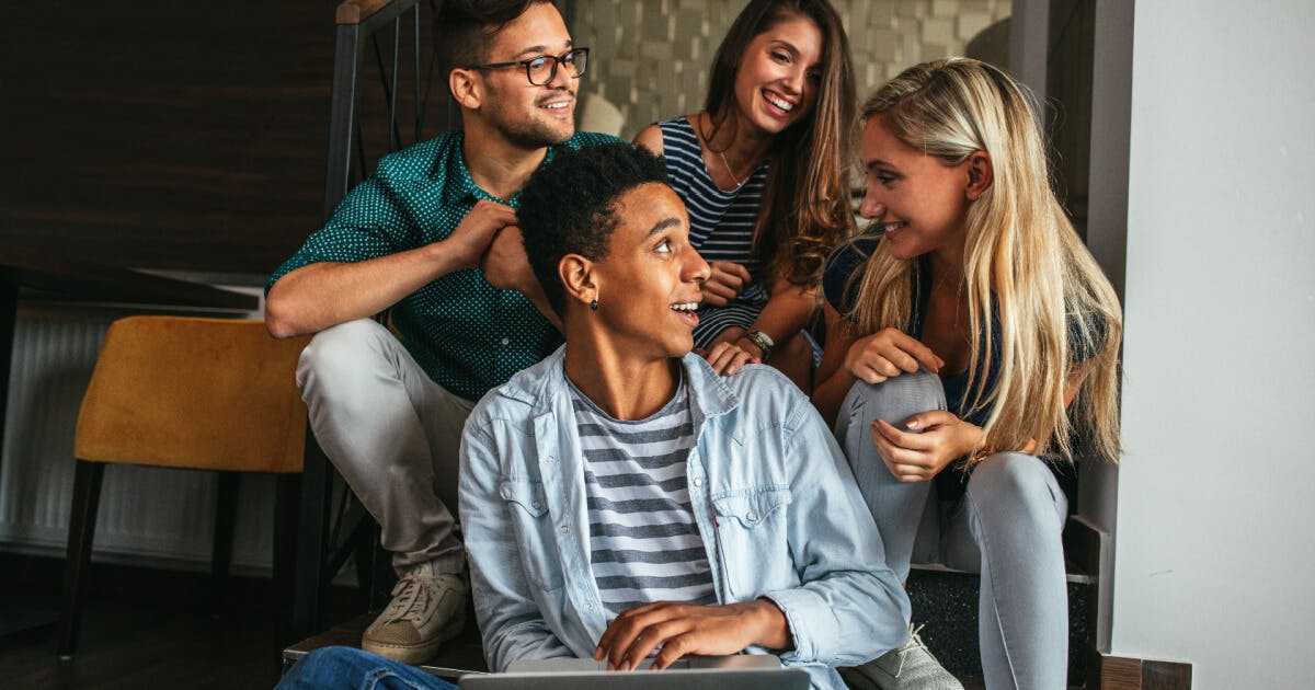 Quatro jovens sentados nas escadas, utilizando um laptop, em um ambiente descontraído e colaborativo.