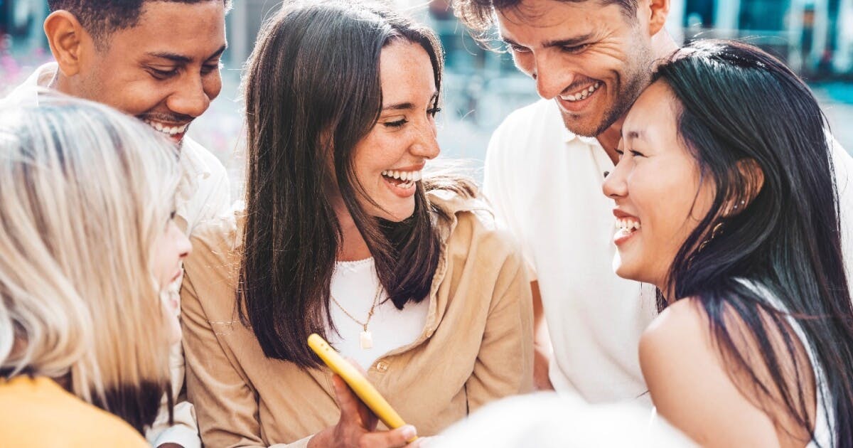 Grupo de pessoas sorrindo enquanto observam um celular, demonstrando alegria e interação social.