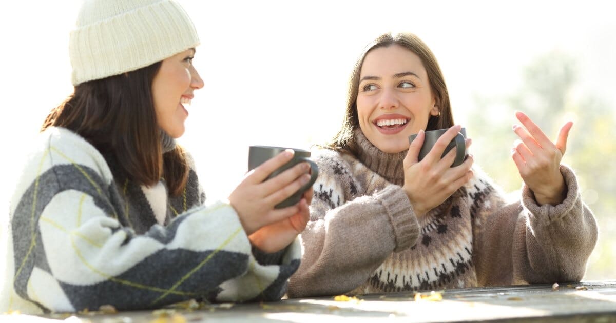 Duas mulheres sentadas em um banco, conversando animadamente em um ambiente ao ar livre.