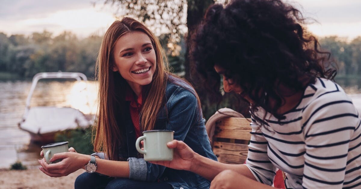 Duas mulheres sentadas em um banco próximo a um lago, desfrutando de um momento de tranquilidade e companhia.