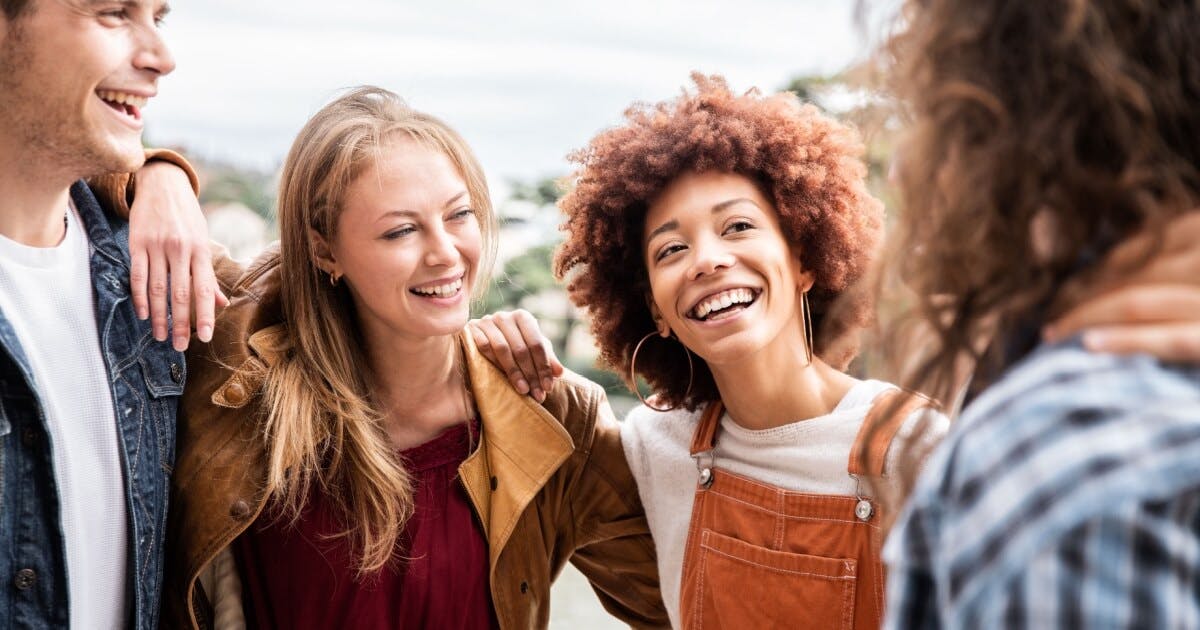 Quatro jovens sorrindo juntos ao ar livre, transmitindo alegria e amizade em um ambiente natural.