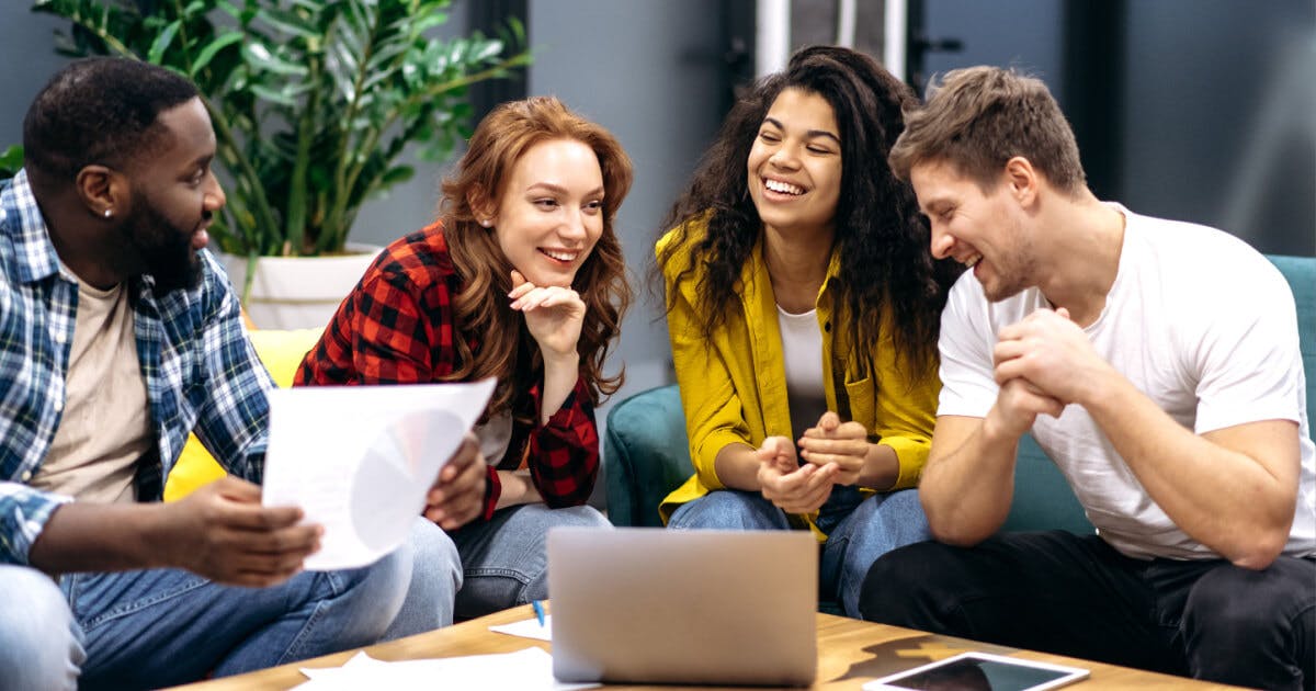 Quatro jovens sentados em torno de uma mesa com um laptop, discutindo e colaborando em um projeto.