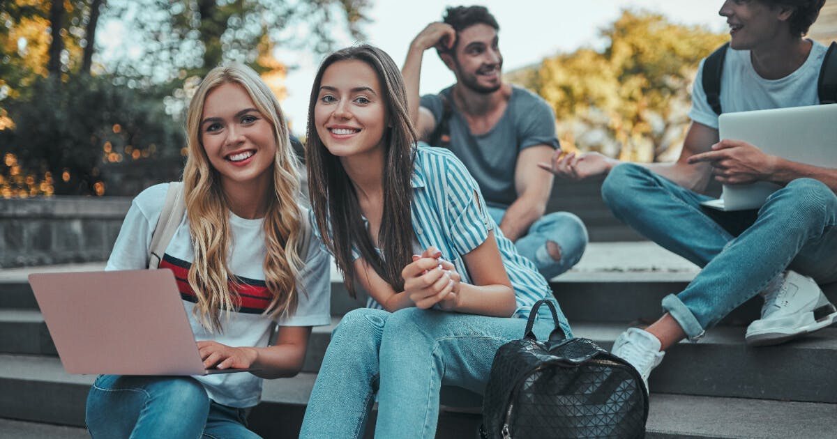 Três jovens sentados em degraus, utilizando laptops, imersos em suas atividades.